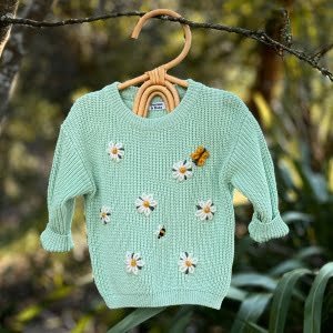 Daisy Design Jumper on clothes hanger with a bush backdrop