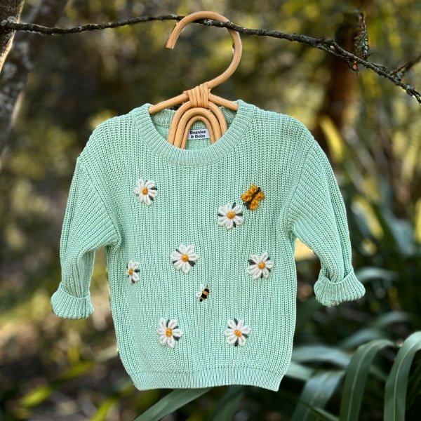 Daisy Design Jumper on clothes hanger with a bush backdrop